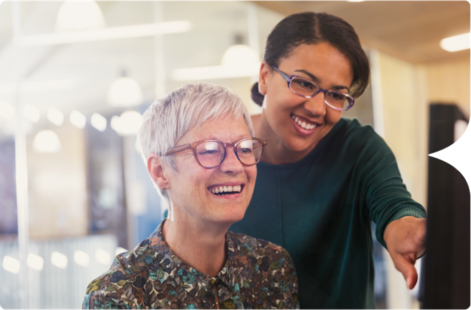 Photograph of an African American woman helping an older Caucasian woman on the computer.